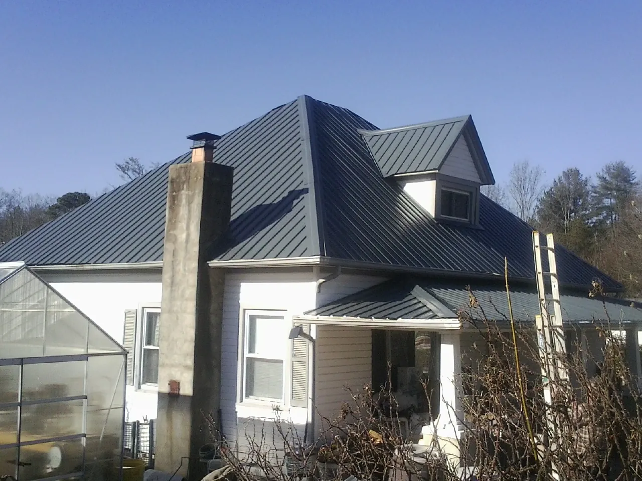 Dark blue standing seam metal roof on a white farmhouse with dormer — Slate & Tile Roof Repair by Roofing Brothers in Keystone