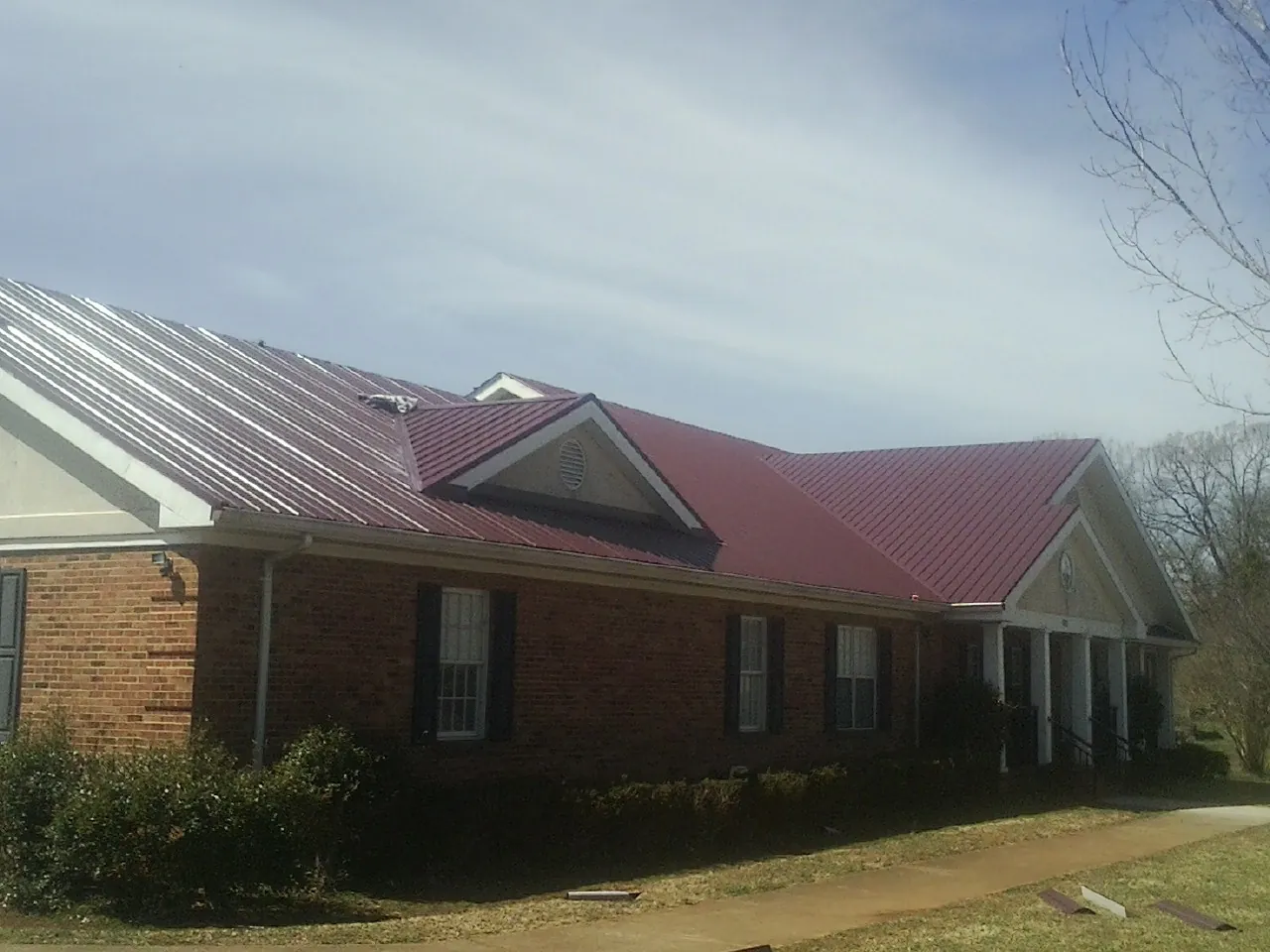 Red metal roof with gabled entries on a long brick building, from a Hail Damage Roof Repair job in Keystone