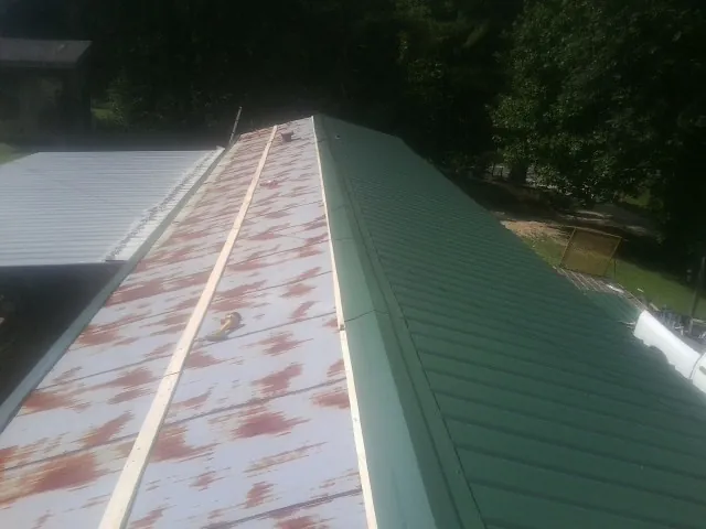 Old rusted panels beside newly installed green metal roofing — Wind Damage Roof Repair by Roofing Brothers in Keystone
