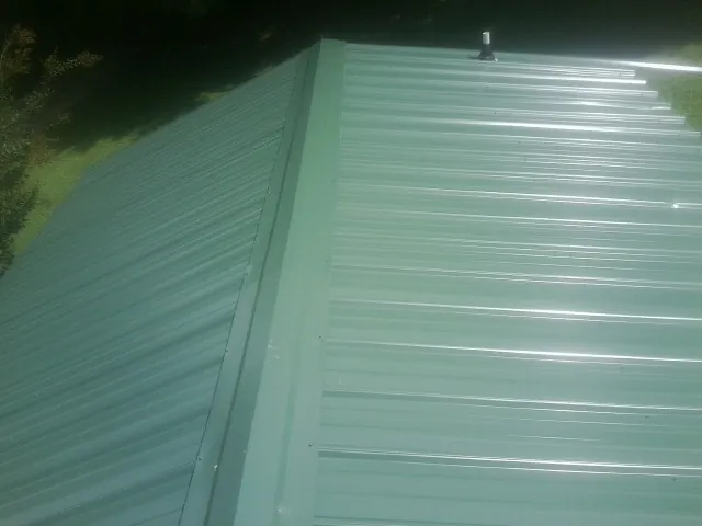 New green metal panels meeting at the ridge of a roof — Flat Roof Repair work by our crew in Keystone